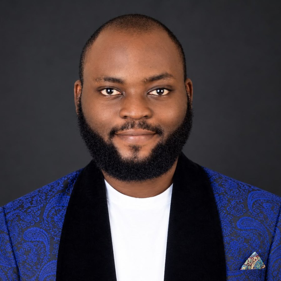 Portrait of Adetokunboh Adesuyi in a blue patterned jacket against a dark grey background.